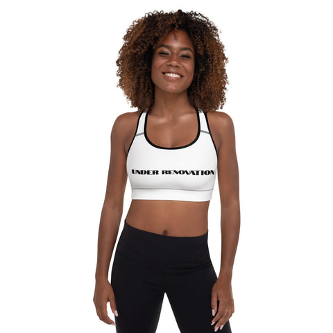 Young woman wearing white sports bra with black trim and the words "Under Renovation" written in black bold letters.